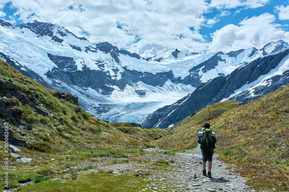 Guy hiking through the valley towards a glacier and mountain range.