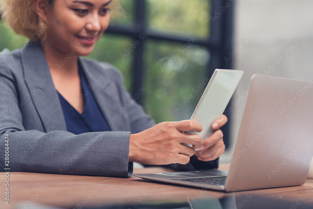 Young woman using smartphone at table with laptop in office Young woman using smartphone at table with laptop in office