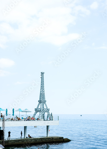 A small copy of the Eiffel tower on the embankment of Yalta, tourists relax on the city beach