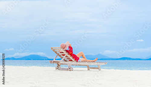 Women wearing a wide-brimmed pink hat Resting happily on a wooden chair by the beach on blue sky © noppadon