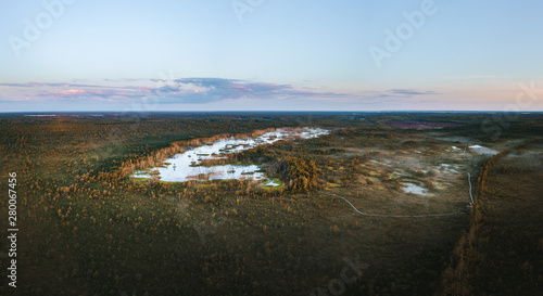 Obraz na płótnie Warmly colored sunrise over a foggy swamp. Aerial view of stunning landscape at peat bog at Cenas Tirelis in Latvia. Wooden trail leading along the lake surrounded by pounds and forest. w salonie