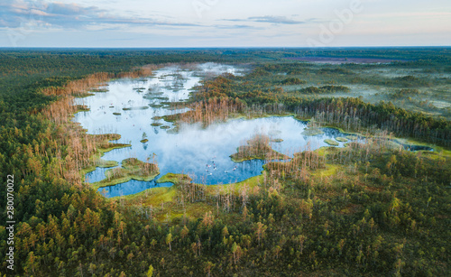 Fototapeta Naklejka Na Ścianę i Meble -  Warmly colored sunrise over a foggy swamp. Aerial view of stunning landscape at peat bog at Cenas Tirelis in Latvia. Wooden trail leading along the lake surrounded by pounds and forest. 