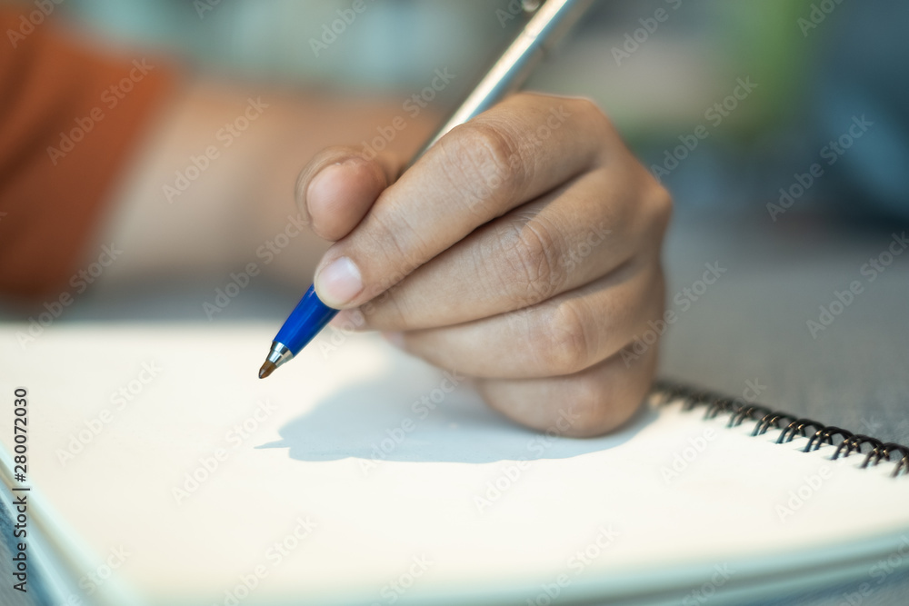 Close up of human hand writing on blank paper note book with a pen. subject is blurred. Close up of human hand writing on blank paper note book with a pen. subject is blurred.