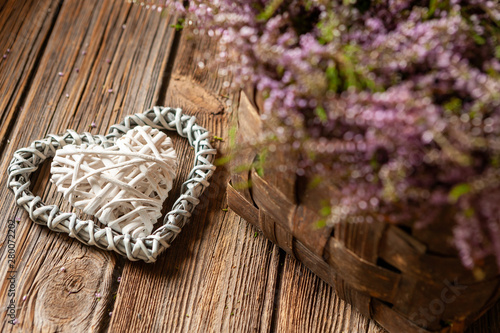 Beautiful fresh bouquet of blooming forest heather in basket and heart symbol on a vintage wooden background.