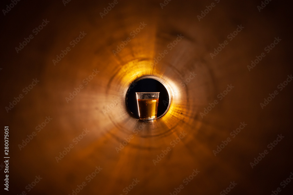 Abstraction a glass of alcohol at the end of the tunnel. Copper red yellow light. A glass with liquid on a black background at the end.