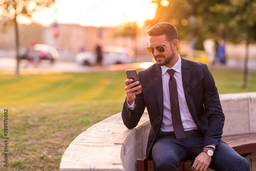 A businessmen sitting on a bench and using his smartphone A businessmen sitting on a bench and using his smartphone