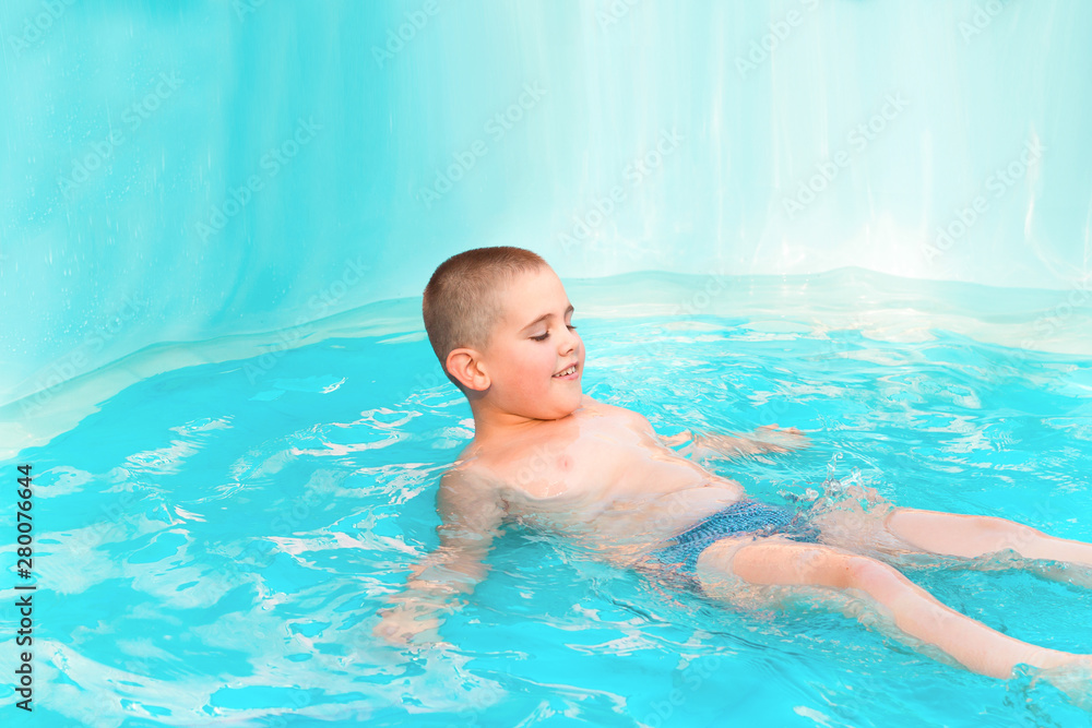 little cute boy swimming in the pool with turquoise water in the summer holidays