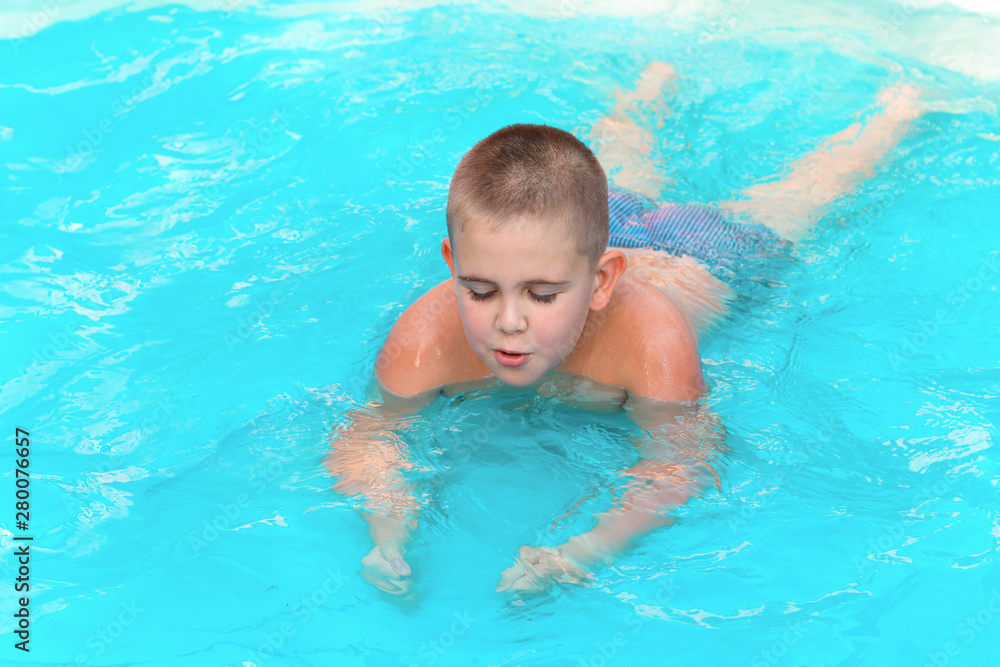 little cute boy swimming in the pool with turquoise water in the summer holidays