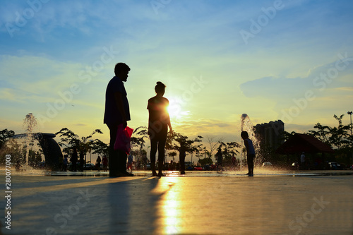 silhouettes of family playing in water fountain at sunset
