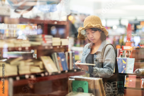 Candid of young hipster college asian woman looking at note book at bookstore. Young asian artist girl standing in retail book shop or stationery store in shopping lifestyle or education concept. photo