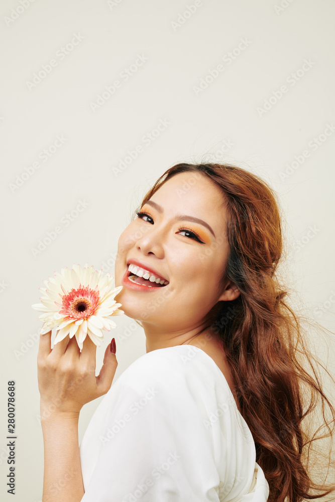 Portrait of Asian model with red long curly hair holding gerbera flower smiling at camera against the white background Portrait of Asian model with red long curly hair holding gerbera flower smiling at camera against the white background