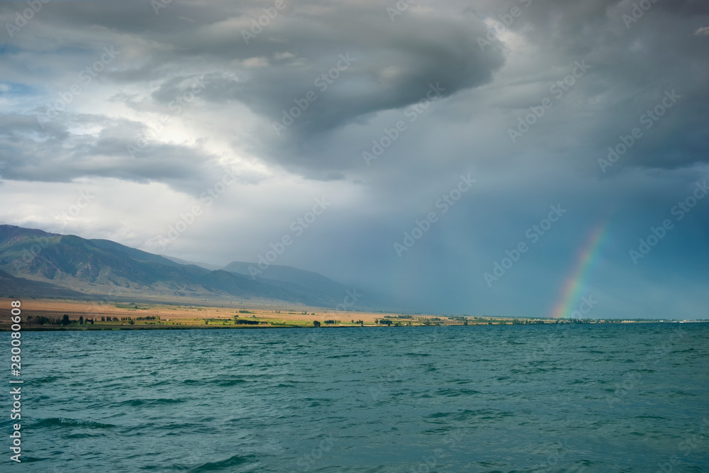 seascape, rainbow after rain against the backdrop of a stormy sky in the evening over the sea and mountains