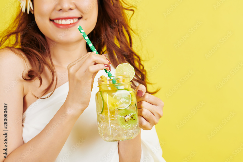 Close-up of young woman smiling while drinking non-alcoholic refreshing drink from drinking straw against the yellow background Close-up of young woman smiling while drinking non-alcoholic refreshing drink from drinking straw against the yellow background