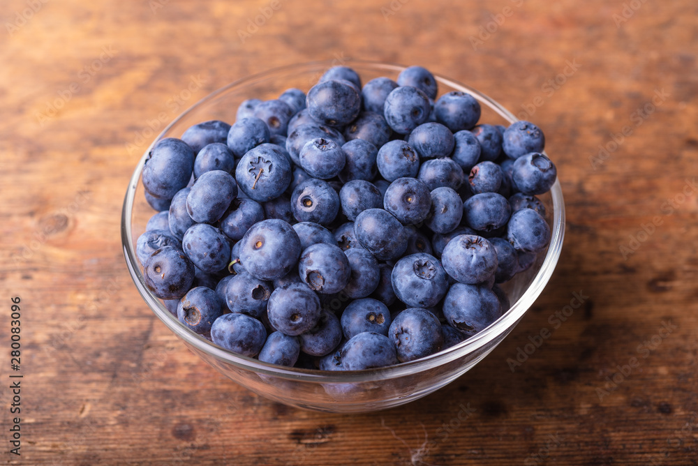 Tasty ripe blueberry berries in a glass cup on a rustic wooden table close-up Tasty ripe blueberry berries in a glass cup on a rustic wooden table close-up