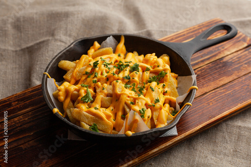Schilderij op canvas Mouthwatering hot french fries with a lot of cheese sauce with herbs in a pan, o