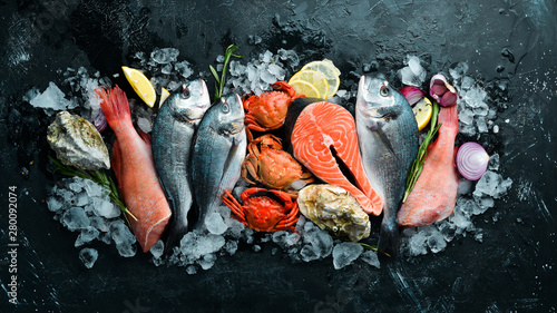 Seafood: Dorado, salmon, crab, grouper, oysters. On a black stone background. Top view. Free space for your text.
