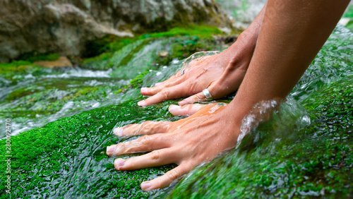 Tanned female hands stroke green moss growing in the clear and transparent water of a mountain river.