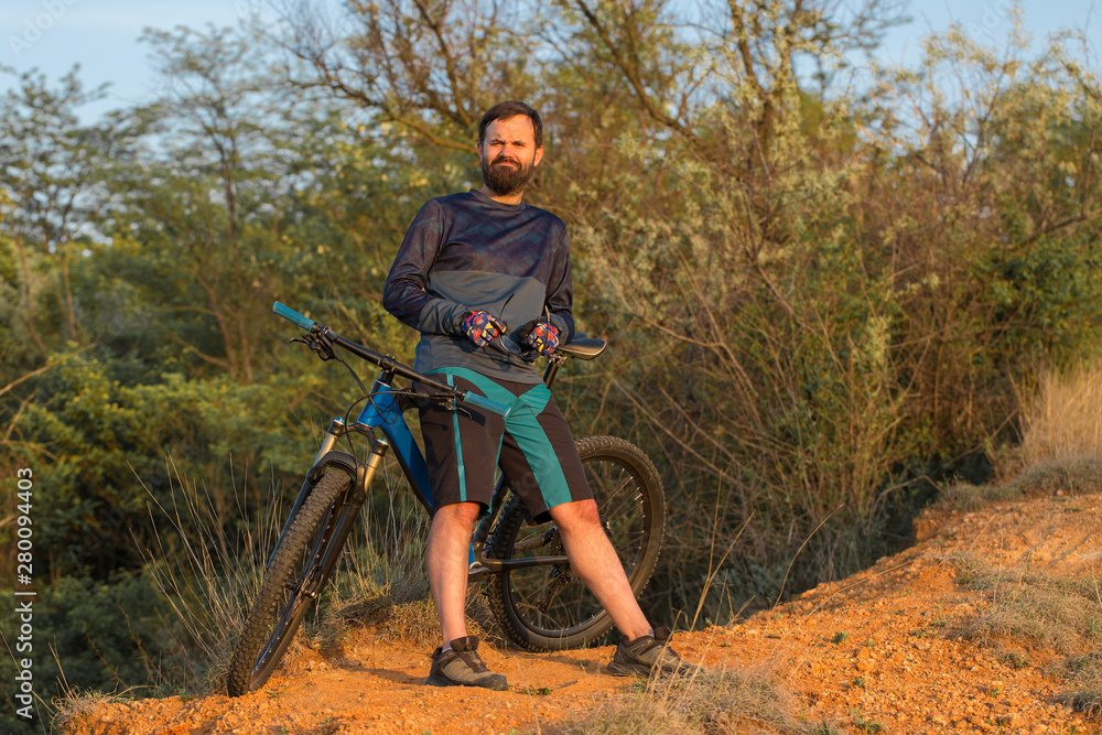 Naklejka premium Cyclist in shorts and jersey on a modern carbon hardtail bike with an air suspension fork rides off-road on the orange-red hills at sunset evening in summer 