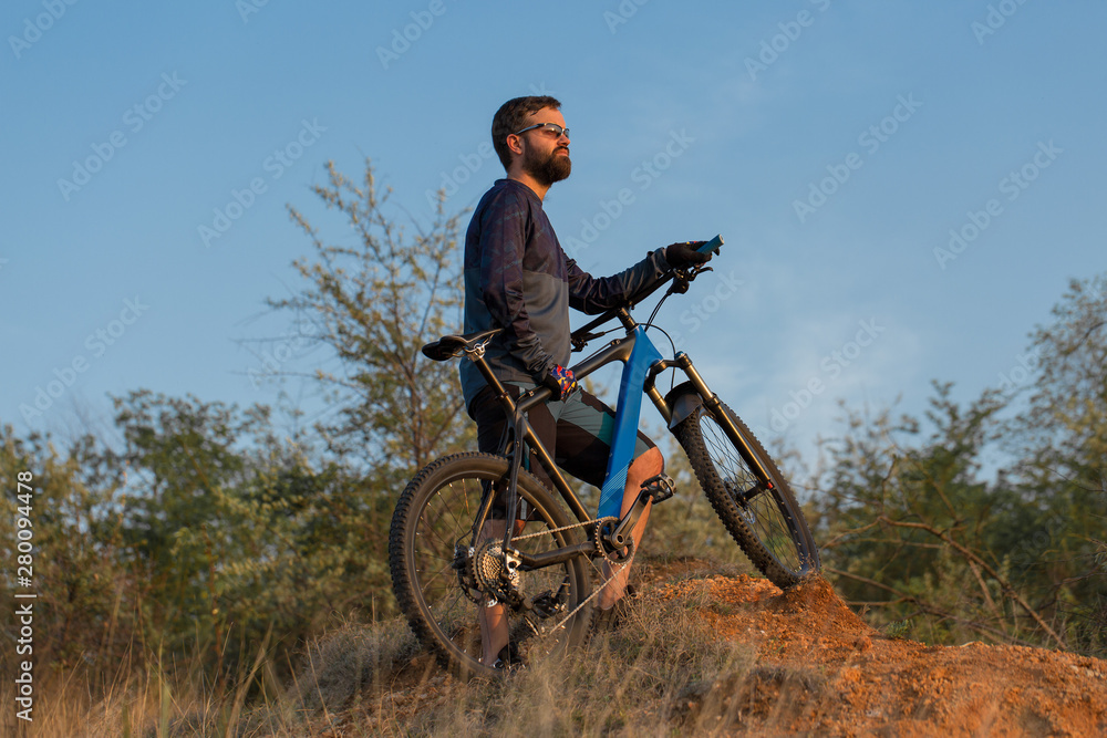 Obraz premium Cyclist in shorts and jersey on a modern carbon hardtail bike with an air suspension fork rides off-road on the orange-red hills at sunset evening in summer