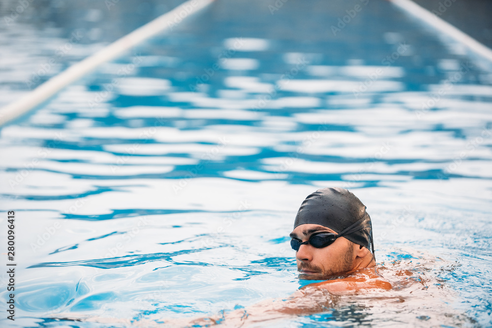 back view of muscular swimmer in swimming cap and goggles standing at swimming pool