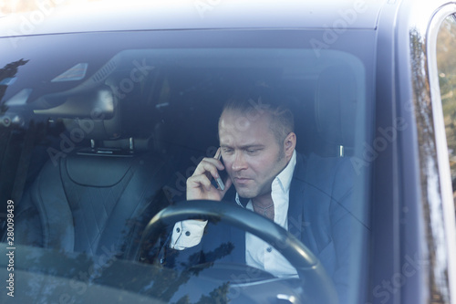 a serious businessman in tha jacket standing sitting in the car holding mobile phone