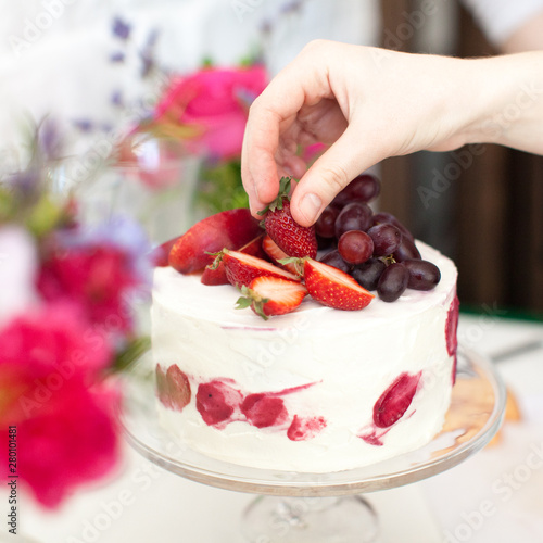 pastry chef hand decorates handmade wedding cake with fruits and berries