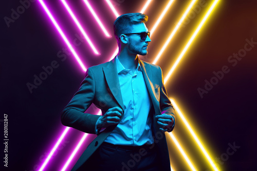 Young handsome model posing in a studio in a trendy neon light. Fashionable man in a stylish suit. Vibrant color. Bright colorful light effects. Disco style. Overlay. Gel filter. Supersaturated