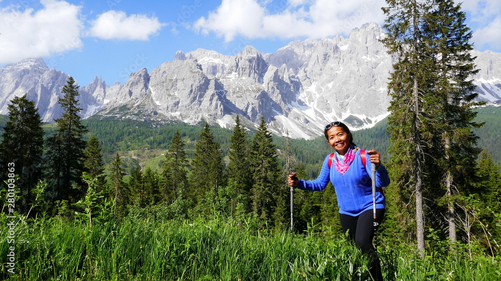 Naklejka premium fröhliche asiatische Touristin wandert durch hohes Gras in den Dolomiten in Südtirol