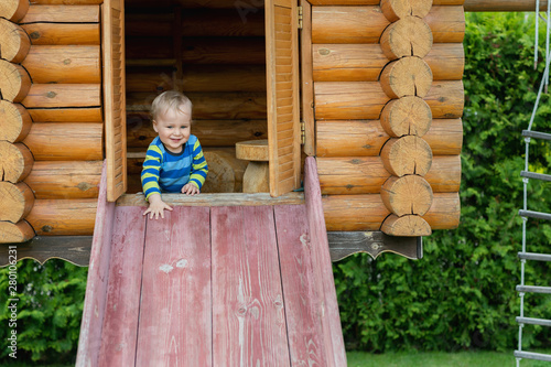 Cute adorable caucasian toddler boy having fun sliding down wooden slide at eco-friendly natural playground at backyard in autumn. Playful funny child portrait enjoying outdoor sport acitivities photo