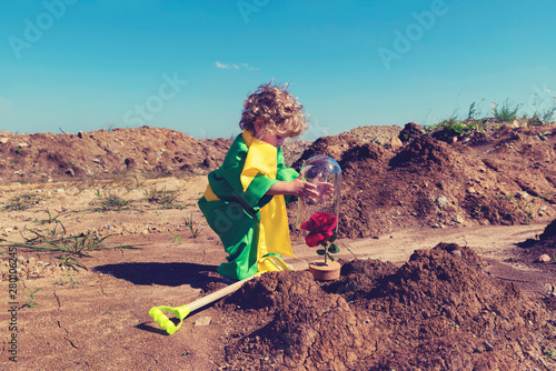 Cute blond toddler boy covers red rose with glass lid in the desert  Little prince concept Selective focus