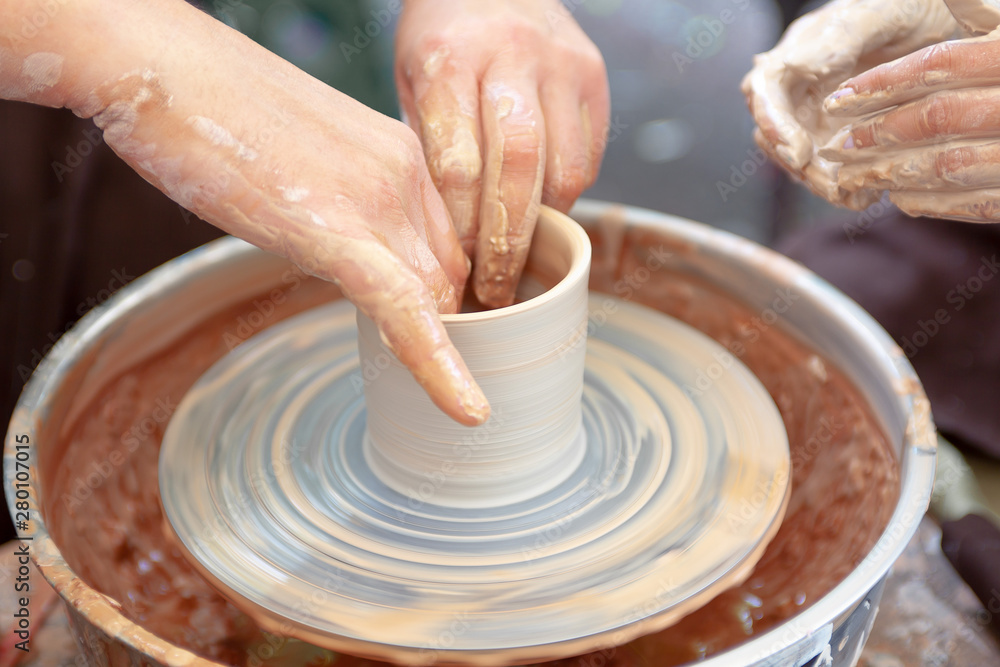 Close up pottery. Adult potter muddy hands guiding child hands to help with clay on a wheel