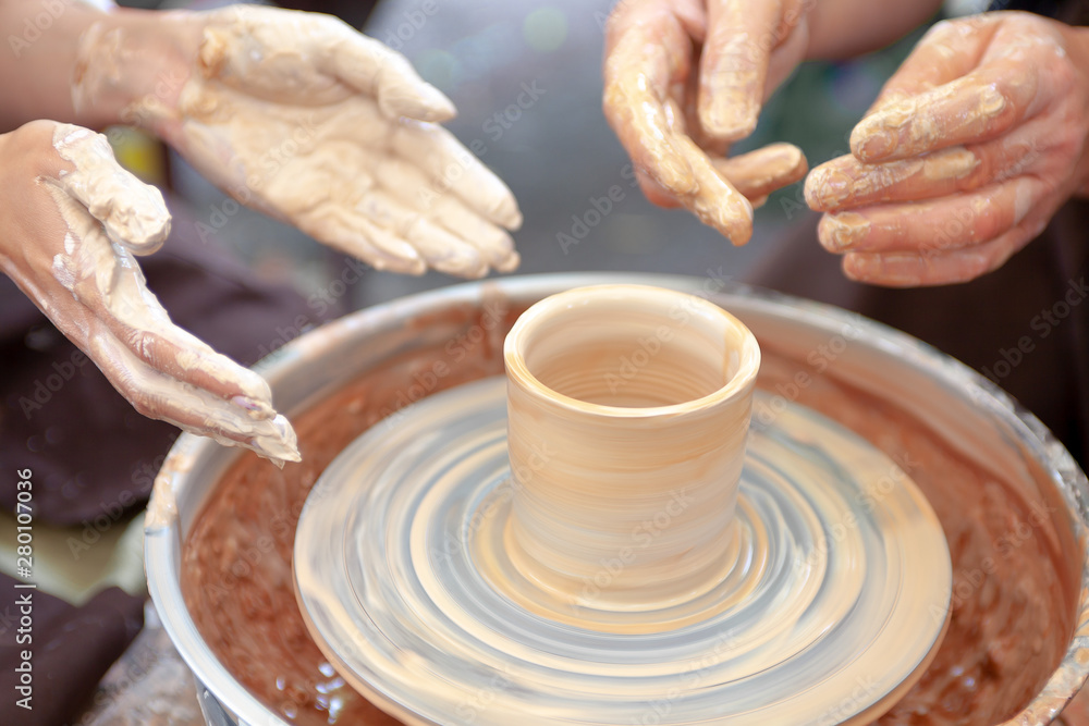 Close up pottery. Selective focus. Adult potter muddy hands guiding child hands to help with clay on a wheel