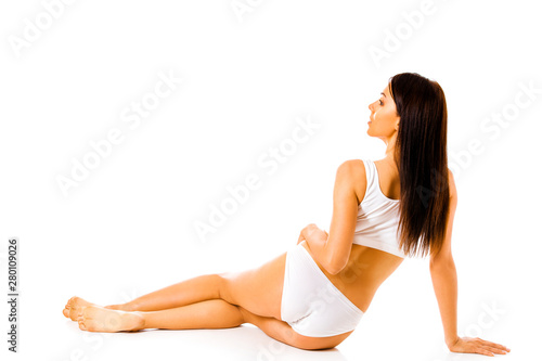 Back view of woman with long hair in underwear sitting on the floor on white background.