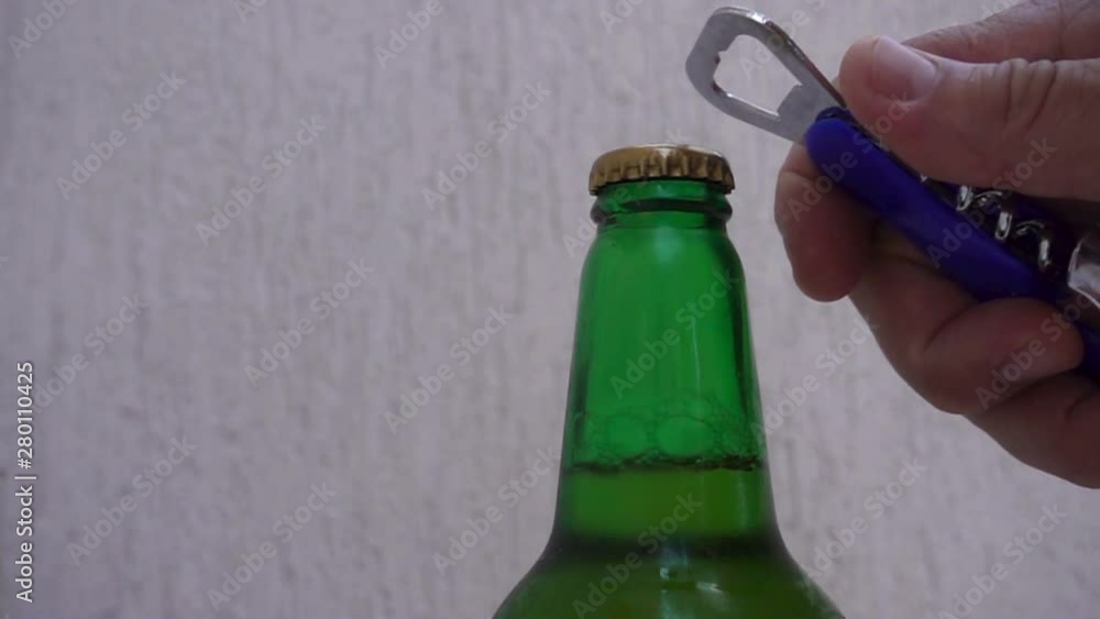 Slow motion hand with opener opens lid on glass beer bottle Slow motion hand with opener opens lid on glass beer bottle
