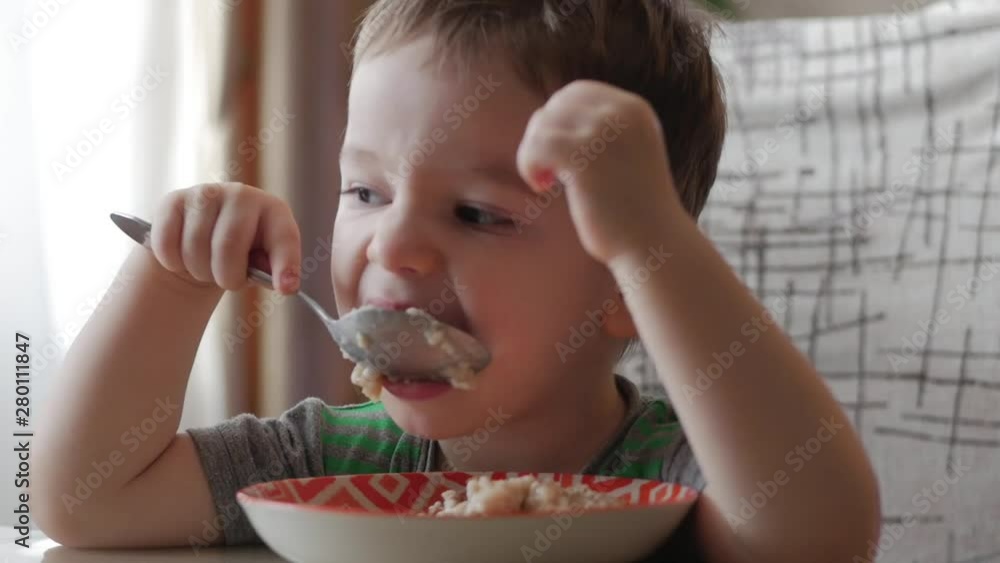 Cute little baby alone eats porridge with a spoon from a plate, the concept of healthy eating. Cute little baby alone eats porridge with a spoon from a plate, the concept of healthy eating.