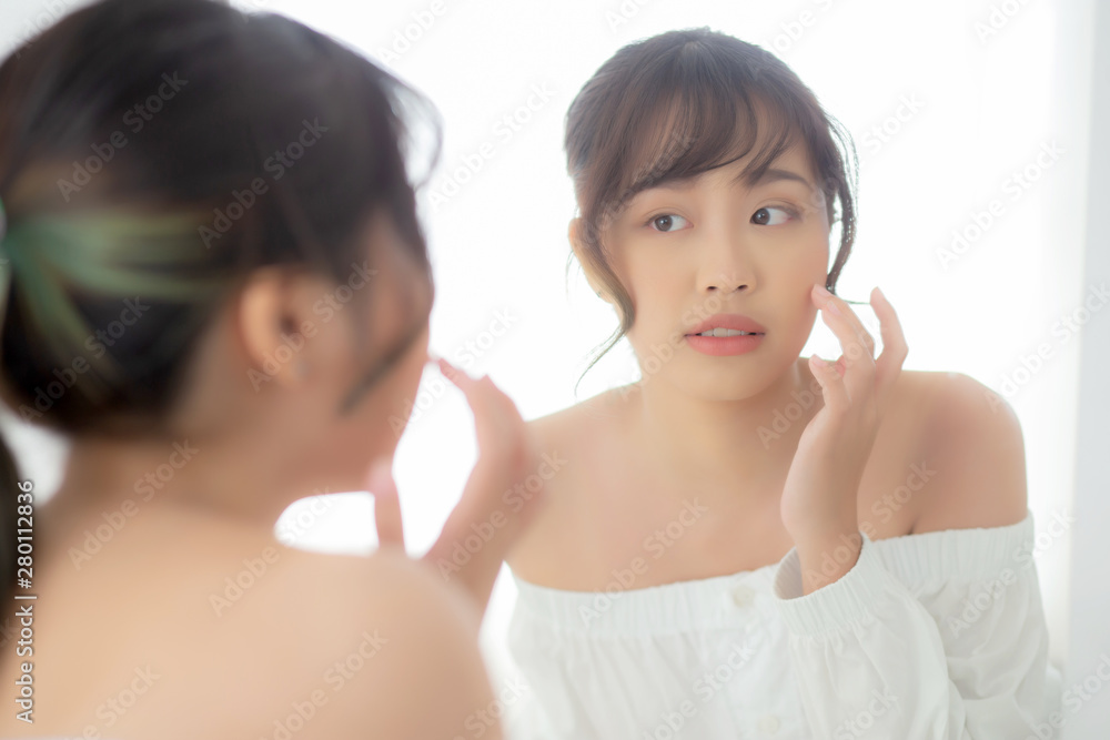 Beauty portrait young asian woman smiling look at mirror of checking skin care caucasian with wellness in the bedroom, beautiful girl happy touching face in reflection for health, lifestyle concept. Beauty portrait young asian woman smiling look at mirror of checking skin care caucasian with wellness in the bedroom, beautiful girl happy touching face in reflection for health, lifestyle concept.