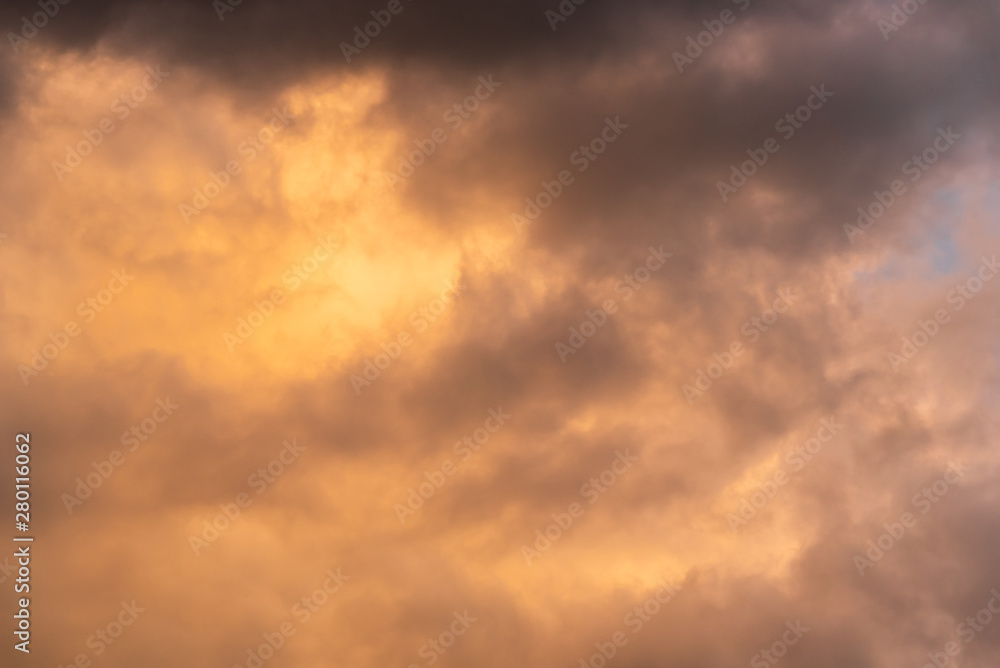 Stormy sky at twilight with clouds in various shades of orange and gray with a hint of blue sky