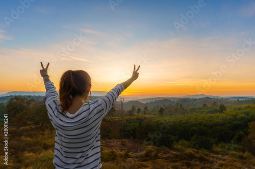 Asian woman standing and hand up in tropical forest and looking far away at sunrise time.