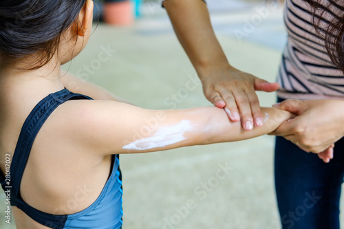 mom applying sunblock lotion on little girl back befor swim