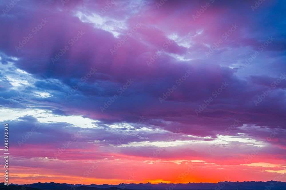 Colorful clouds at sunset over an urban environment with mountains in the distance