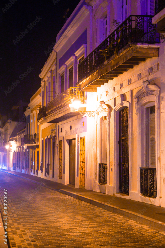Empty street scene from Old San Juan Puerto Rico at night with buildings and cobblestones. 