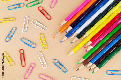 Lots of colorful pencils and paper clips on a nice beige background