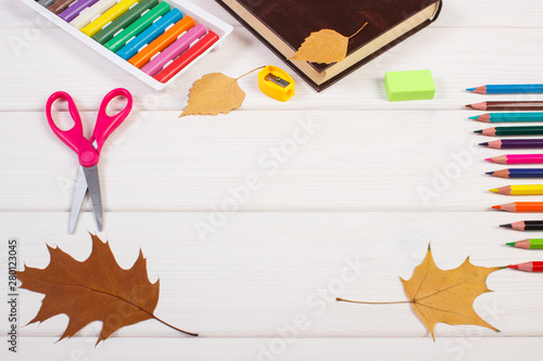 Frame of school accessories, book and autumnal leaves on boards. Back to school concept