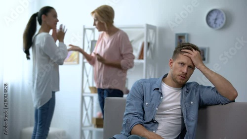 Exhausted male listening wife and mother-in-law arguing at home, rivalry