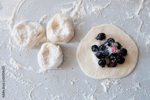 On the table, sprinkled with flour, a circle of dough is rolled out with a filling in the middle, irgi berries.Cutting test. Cooking dumplings or ravioli with fresh berries concept. © Svetlana