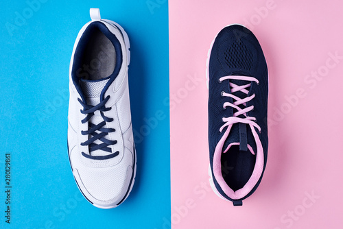 male and female sport shoes on a pastel blue and pink background, top view. Minimal fashion style