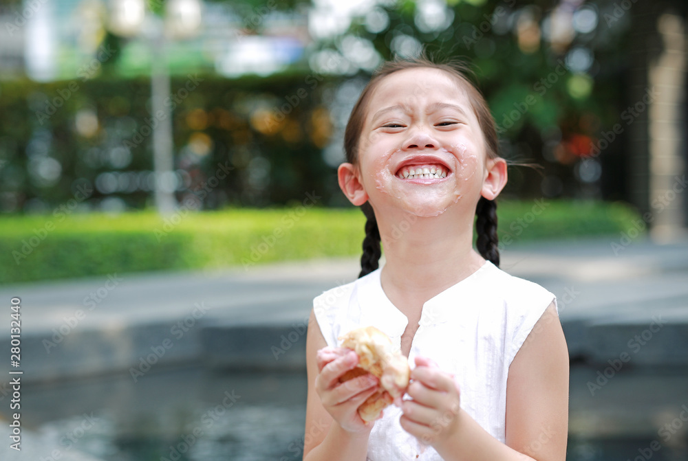 Happy Asian little girl eating bread with Stuffed Strawberry-filled dessert and Stained around her mouth in garden outdoor. Happy Asian little girl eating bread with Stuffed Strawberry-filled dessert and Stained around her mouth in garden outdoor.