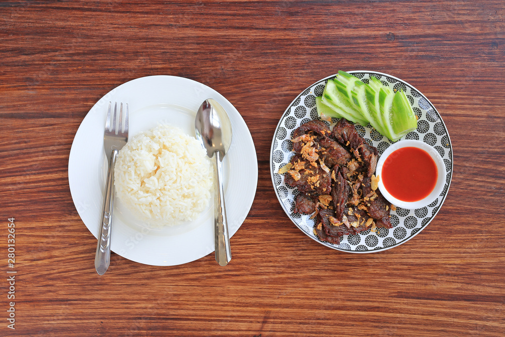 Deep fried beef served with sliced cucumber and sweet chili sauce served with jasmine rice on wooden board background.