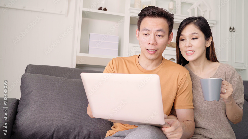 Asian couple using laptop and drinking warm cup of coffee in living room at home, sweet couple enjoy love moment while lying on the sofa when relax at home. Lifestyle couple relax at home concept. Asian couple using laptop and drinking warm cup of coffee in living room at home, sweet couple enjoy love moment while lying on the sofa when relax at home. Lifestyle couple relax at home concept.