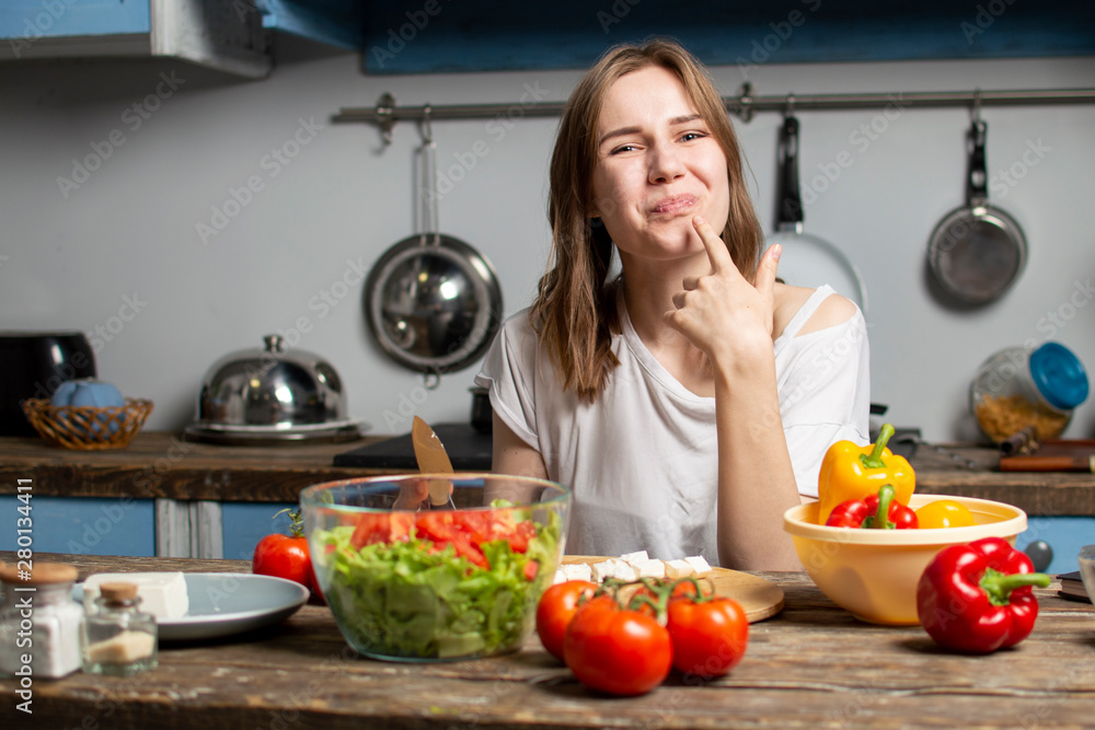 young girl prepares a vegetarian salad in the kitchen, she licks her finger and tastes, the process of preparing healthy food